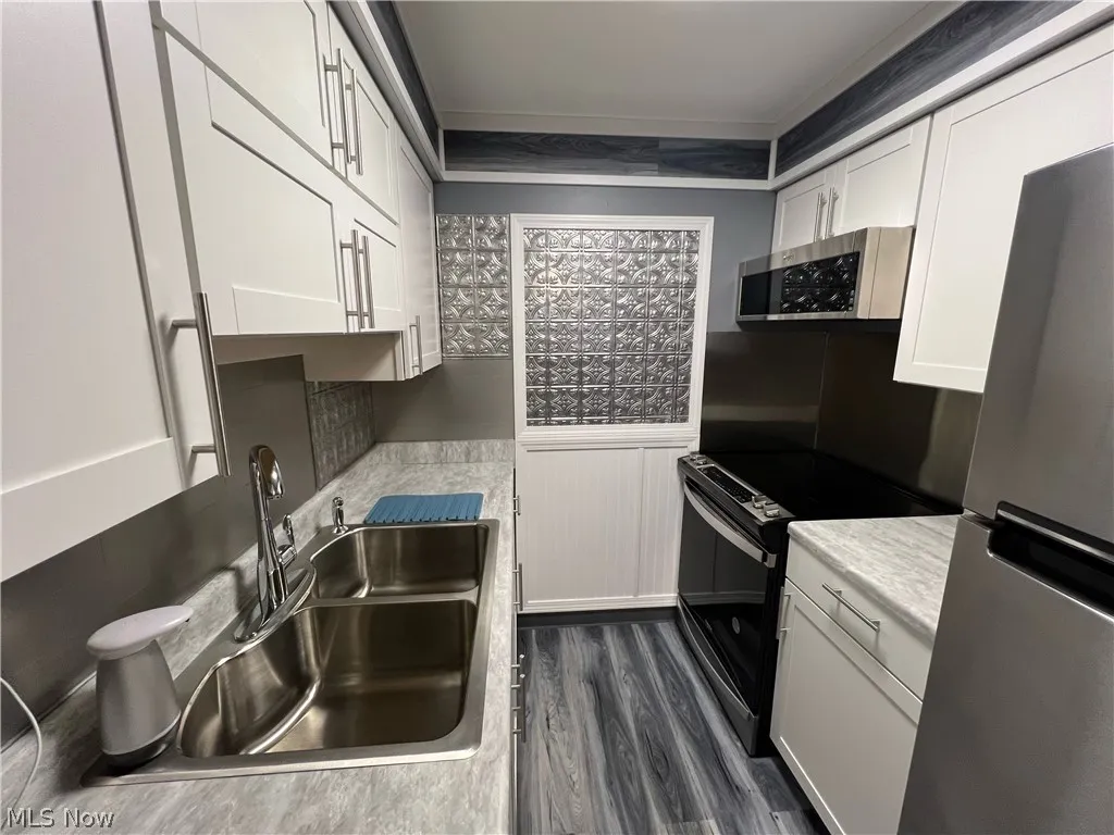 Kitchen with appliances with stainless steel finishes, sink, dark wood-type flooring, and white cabinetry