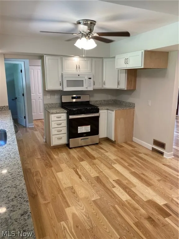 Kitchen with light hardwood / wood-style flooring, white cabinets, light stone counters, ceiling fan, and gas range