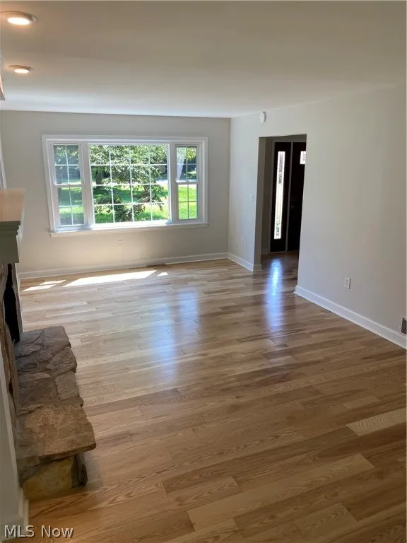 Unfurnished living room featuring a healthy amount of sunlight, a stone fireplace, and hardwood / wood-style floors