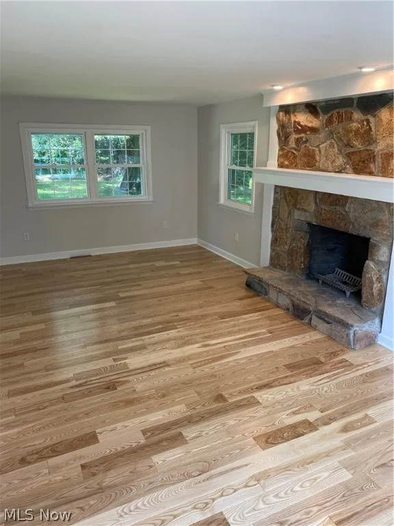 Unfurnished living room with a stone fireplace and light wood-type flooring