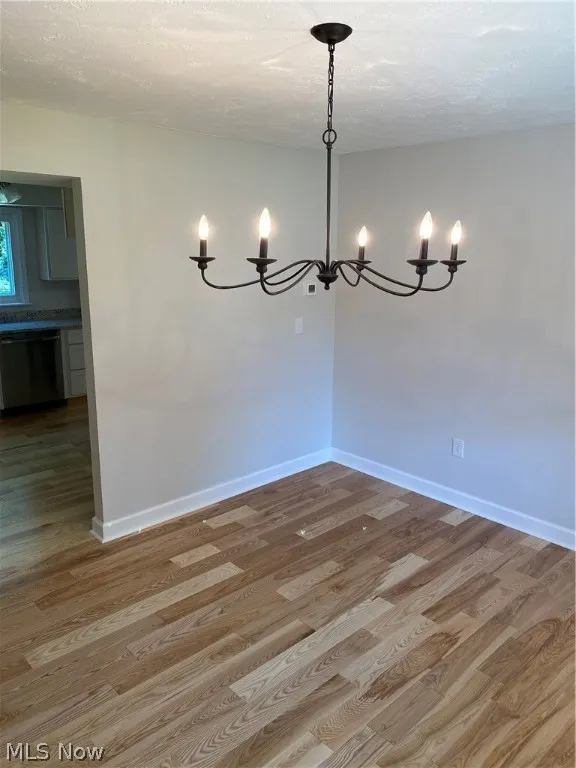 Unfurnished room with a textured ceiling, hardwood / wood-style flooring, and a notable chandelier