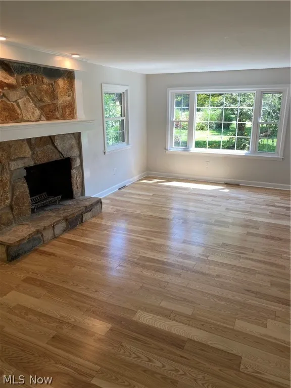 Unfurnished living room with a stone fireplace and hardwood / wood-style floors