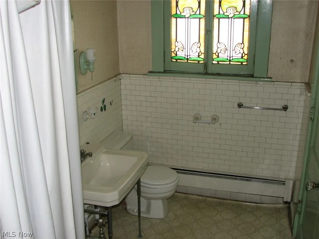 upstairs Bathroom with tile patterned flooring, toilet, tile walls, baseboard heating, and sink