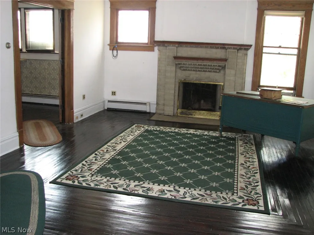 featuring dark hardwood / wood-style floors, a healthy amount of sunlight, a baseboard radiator, and a fireplace