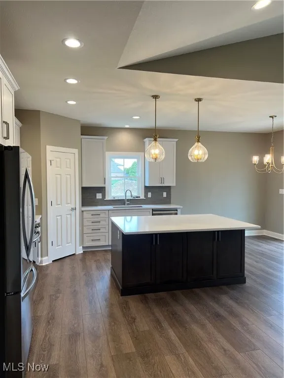 Kitchen with fridge, light countertops, a kitchen island, dark wood-type flooring, and white cabinetry