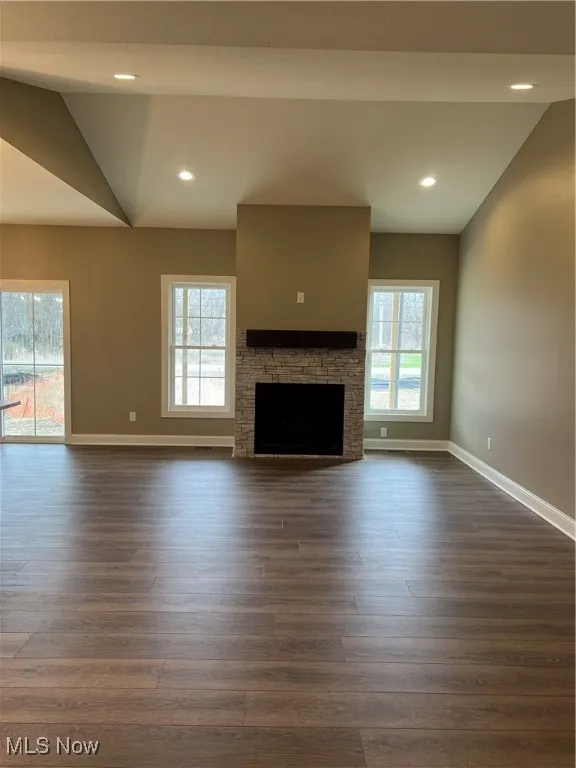 Unfurnished living room featuring dark wood-style flooring, a fireplace, recessed lighting, and lofted ceiling