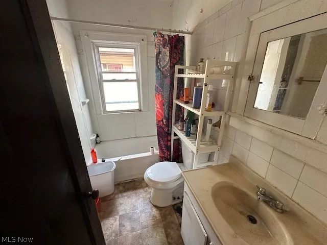 Full bathroom with vanity, tile walls, shower / bath combination with curtain, toilet, and tile patterned flooring