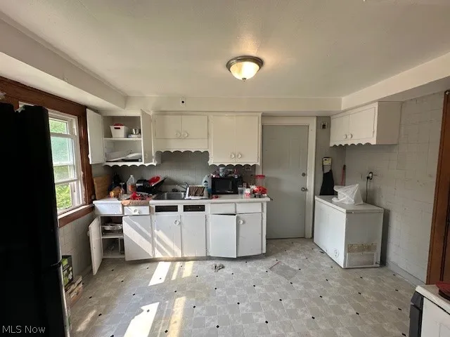 Kitchen with white cabinets, sink, black fridge, and light tile patterned floors