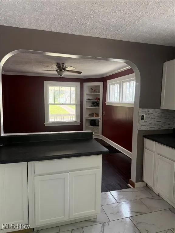 Kitchen featuring arched walkways, dark countertops, a textured ceiling, ceiling fan, and white cabinetry