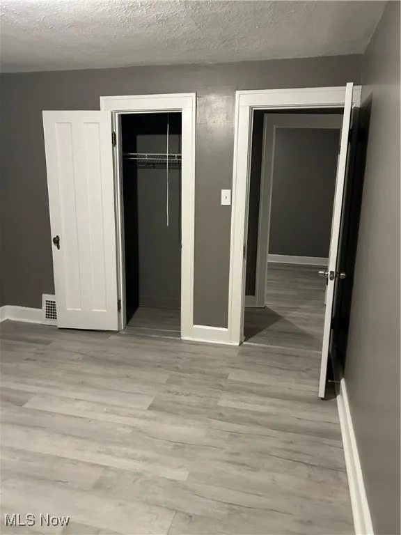 Unfurnished bedroom featuring light wood-style floors, a closet, and a textured ceiling