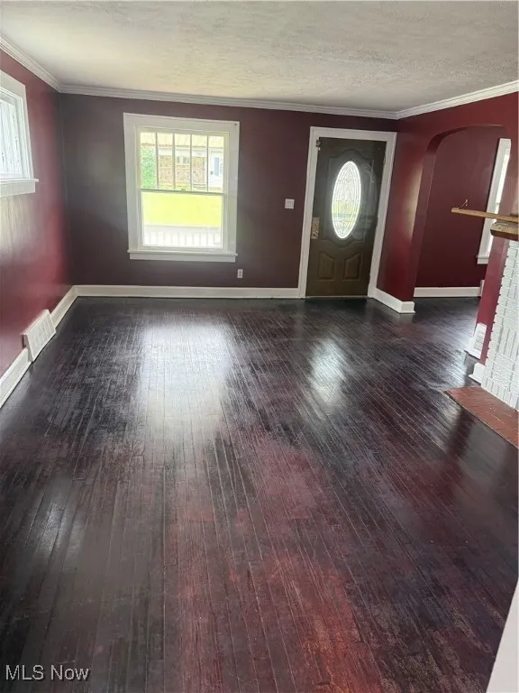 Entrance foyer with wood-type flooring, arched walkways, crown molding, and a textured ceiling