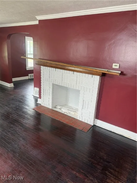 Detailed view of a brick fireplace, ornamental molding, wood finished floors, arched walkways, and a textured ceiling