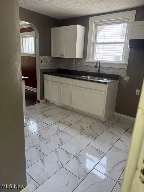 Kitchen with light marble finish floors, a textured ceiling, arched walkways, and white cabinetry