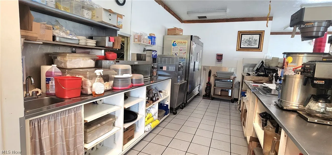 Kitchen featuring light tile patterned flooring, crown molding, sink, stainless steel fridge, and stainless steel counters