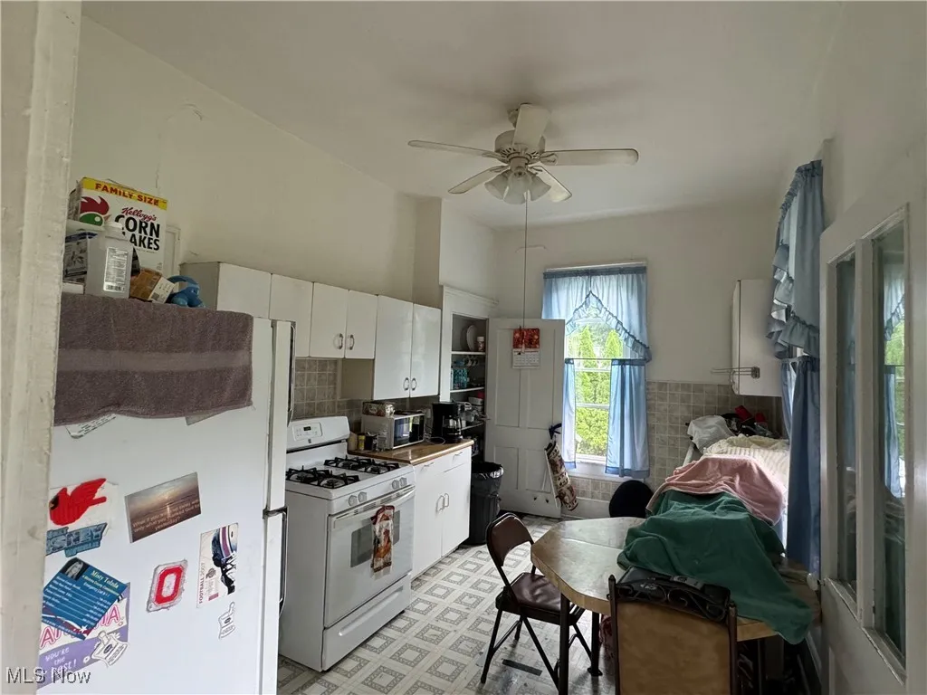 Kitchen featuring white appliances, light tile patterned floors, white cabinets, backsplash, and ceiling fan