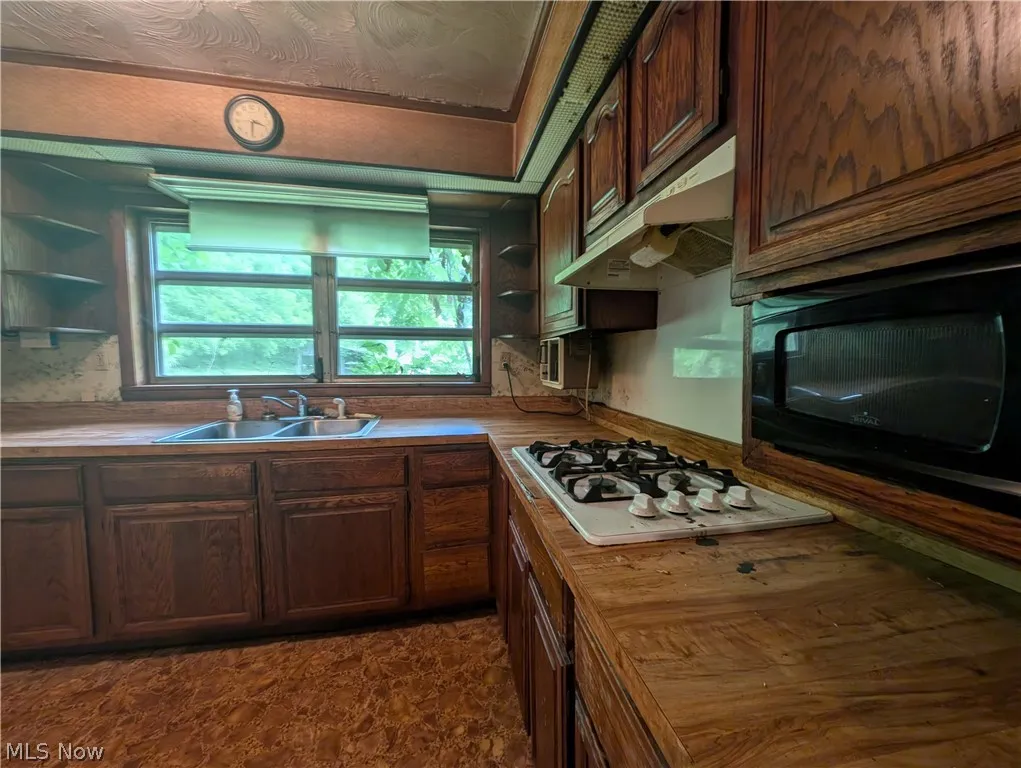 Kitchen with sink, butcher block countertops, white gas cooktop, and dark brown cabinetry