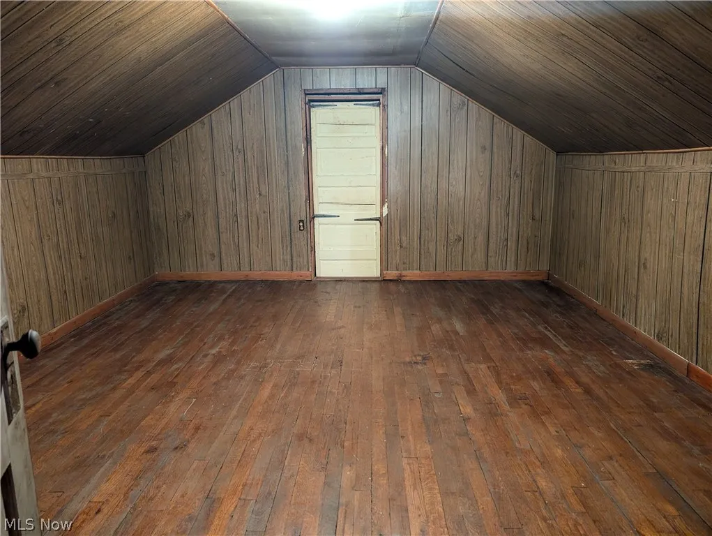 Bonus room featuring dark hardwood / wood-style floors, wooden walls, and vaulted ceiling