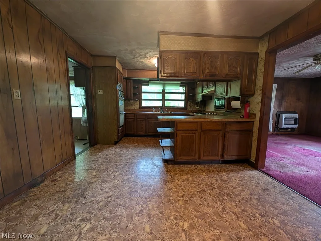 Kitchen featuring wooden walls, sink, ceiling fan, built in microwave, and double oven