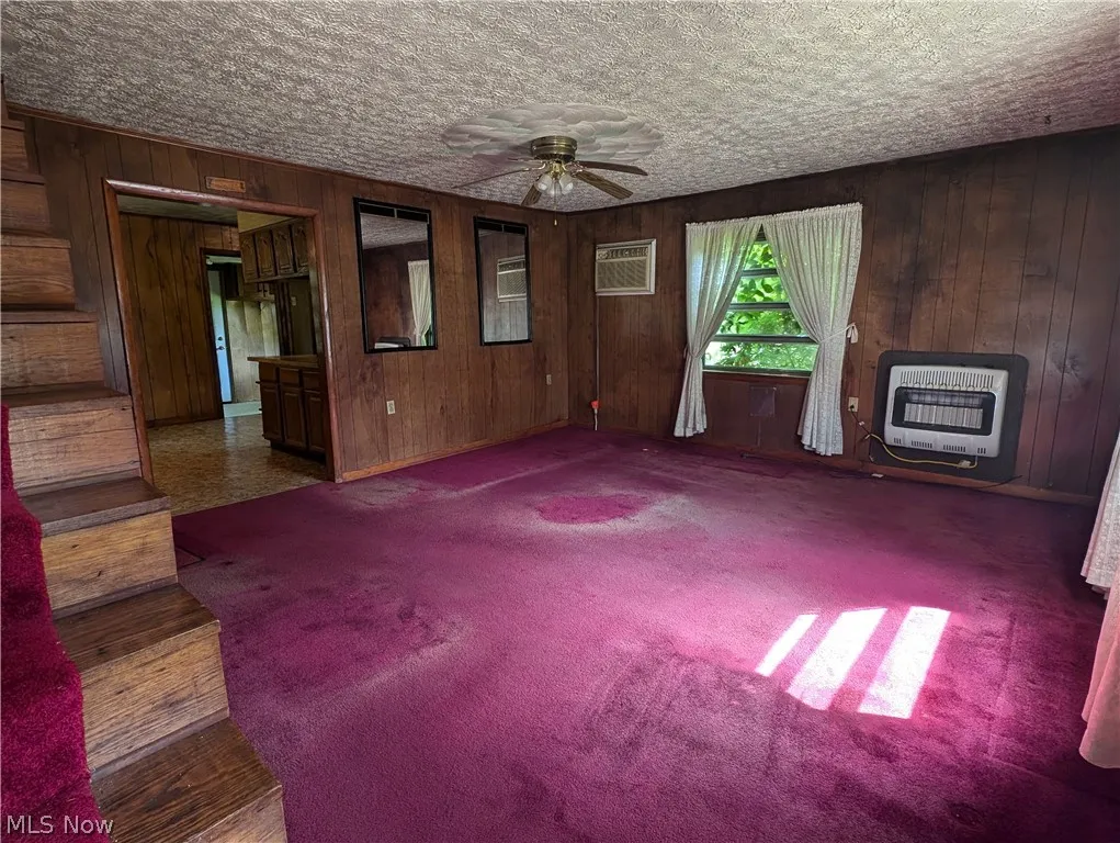 Unfurnished living room with heating unit, a wall mounted air conditioner, ceiling fan, a wood stove, and hardwood / wood-style floors
