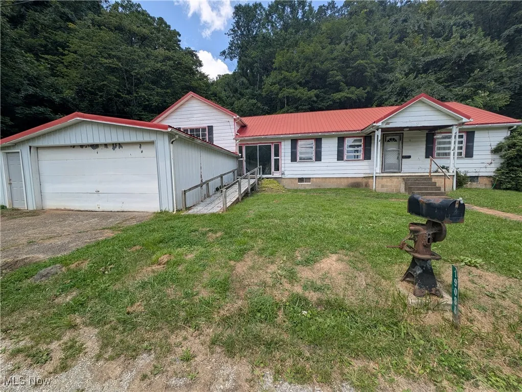 View of front of property with a metal roof, a garage, a front yard, driveway, and a wooded view