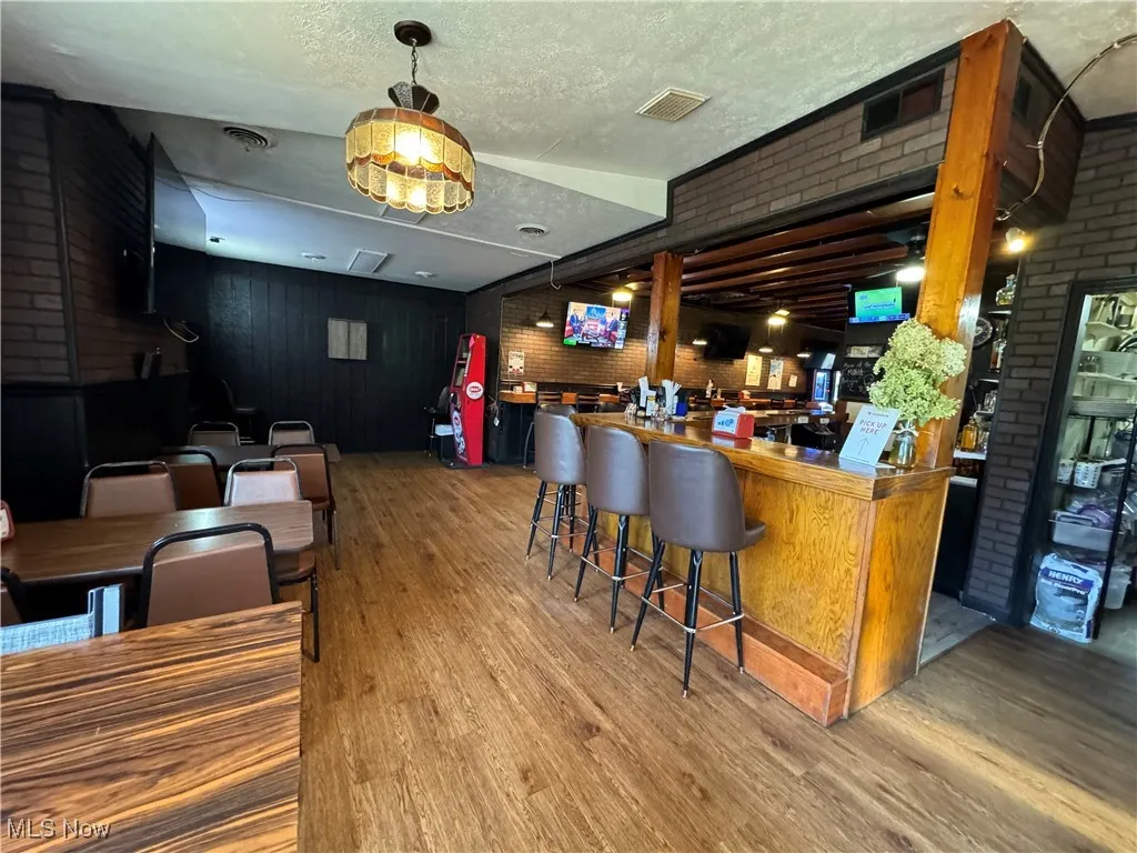 Bar featuring a textured ceiling, hardwood / wood-style flooring, and brick wall