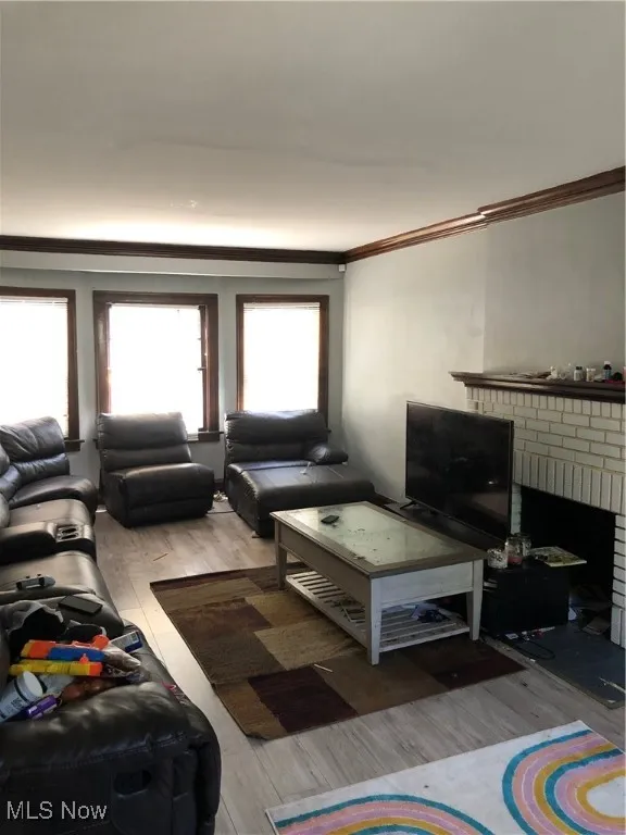 Living room featuring ornamental molding, a brick fireplace, and hardwood / wood-style flooring