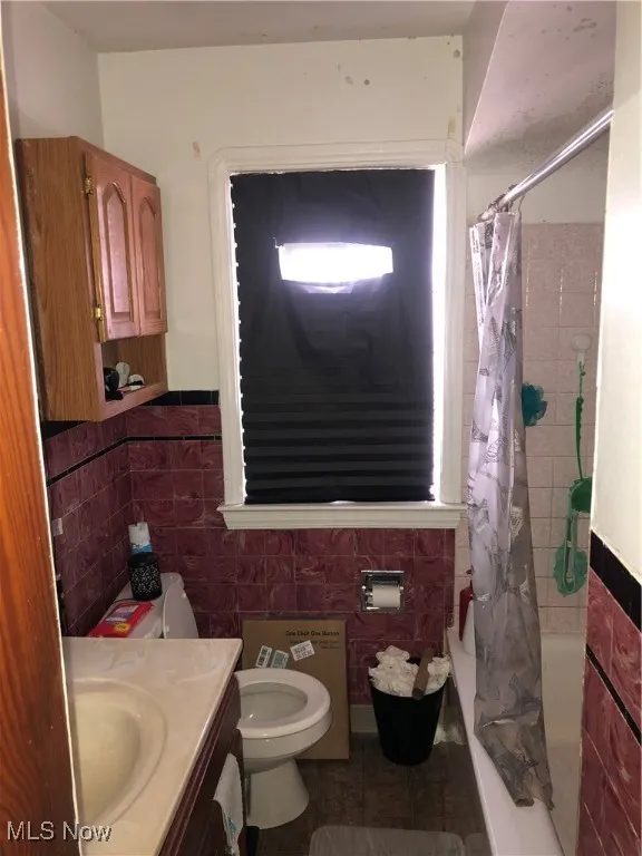 Full bathroom with toilet, vanity, tile walls, tile patterned floors, and shower / bath combo