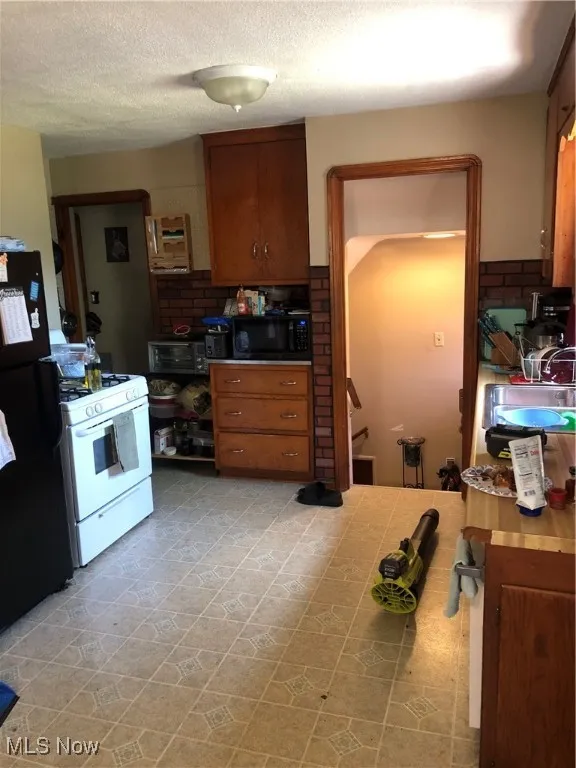 Kitchen with stove, sink, backsplash, light tile patterned floors, and refrigerator