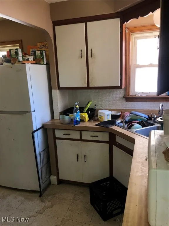 Kitchen featuring refrigerator, white cabinetry, sink, and light tile patterned floors