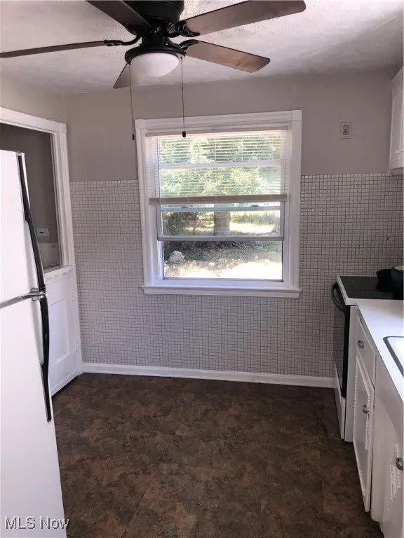 Kitchen with white cabinetry, ceiling fan, dark tile patterned floors, fridge, and stove
