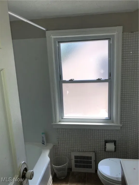 Bathroom with plenty of natural light, tile patterned flooring, toilet, and tile walls