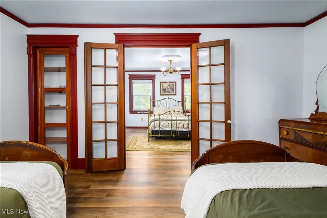 Bedroom featuring dark hardwood / wood-style flooring, an inviting chandelier, french doors, and crown molding