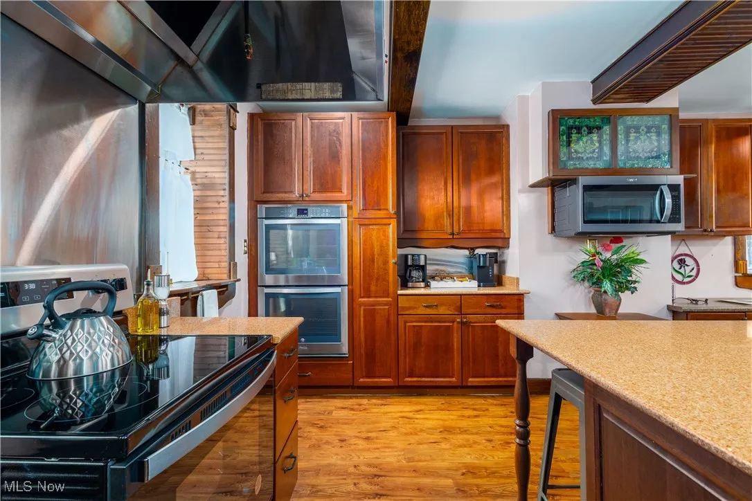 Kitchen featuring appliances with stainless steel finishes, light hardwood / wood-style flooring, light stone counters, and wall chimney range hood