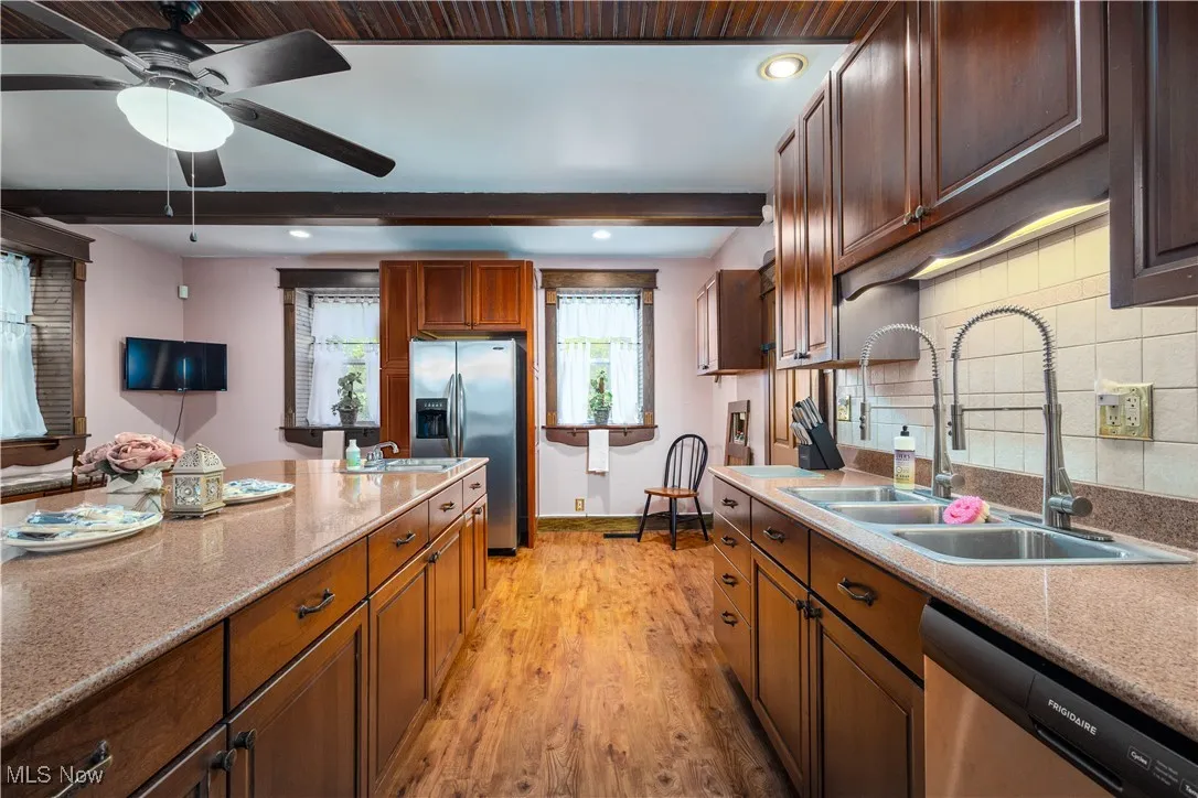 Kitchen with appliances with stainless steel finishes, sink, decorative backsplash, light wood-type flooring, and ceiling fan