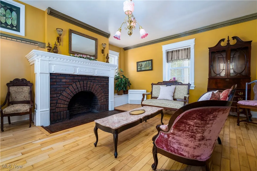 Living room featuring light hardwood / wood-style floors, an inviting chandelier, a brick fireplace, and crown molding