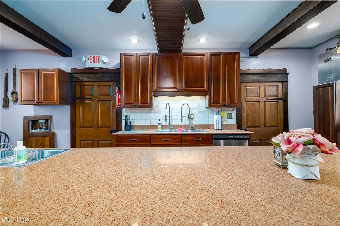 Kitchen featuring sink, stainless steel dishwasher, beamed ceiling, and ceiling fan