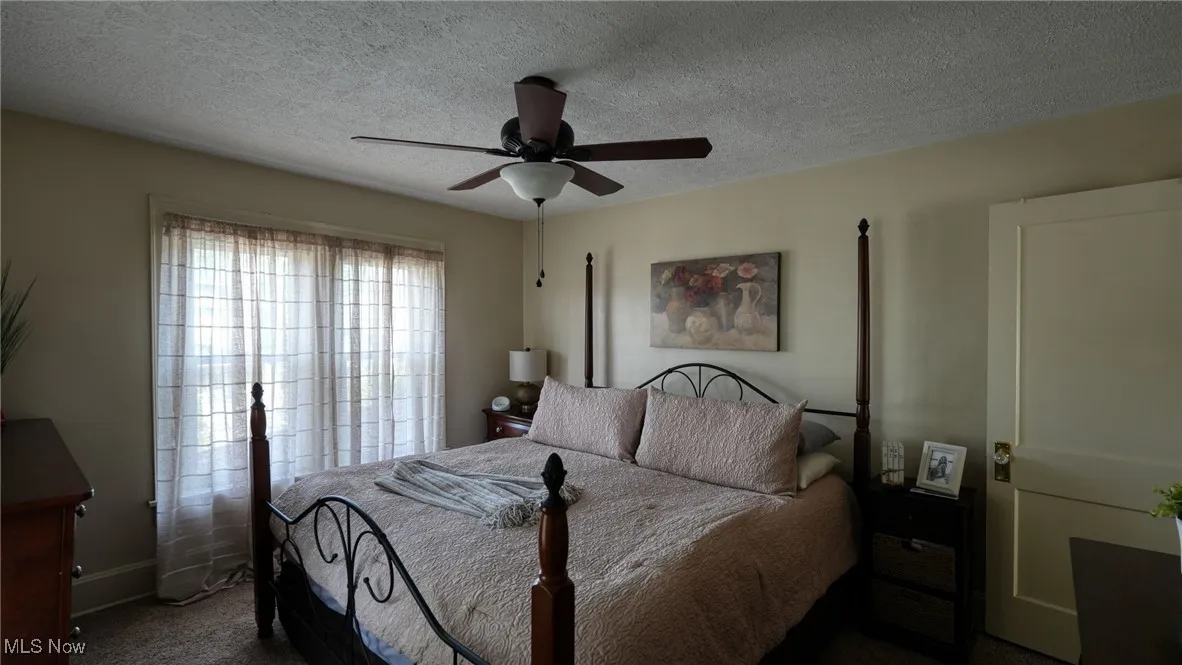 Carpeted bedroom with ceiling fan and a textured ceiling