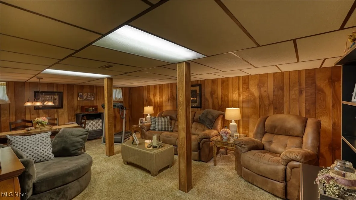Living room featuring carpet floors, wooden walls, and a paneled ceiling