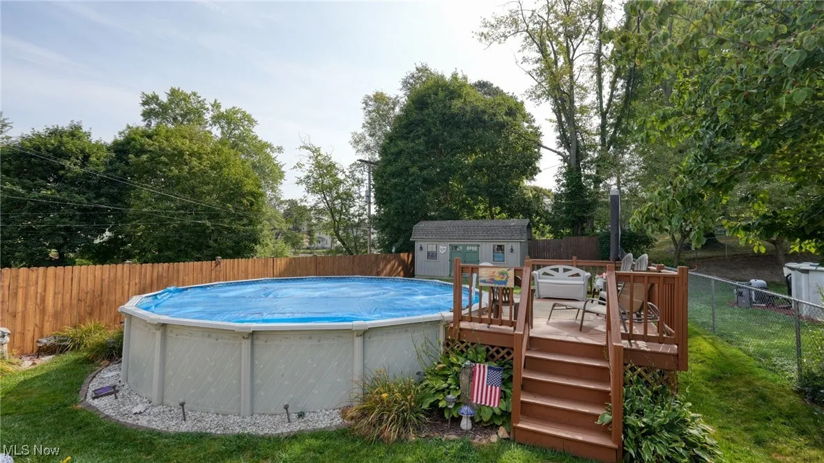 View of pool with a lawn, a wooden deck, and a shed