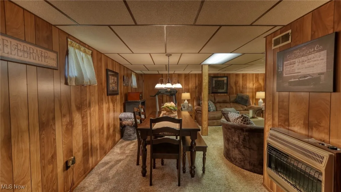 Carpeted dining room featuring a paneled ceiling, wooden walls, and heating unit