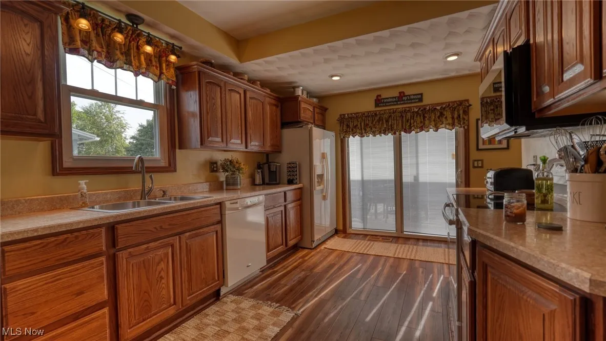 Kitchen featuring sink, dark hardwood / wood-style flooring, light stone countertops, and white appliances