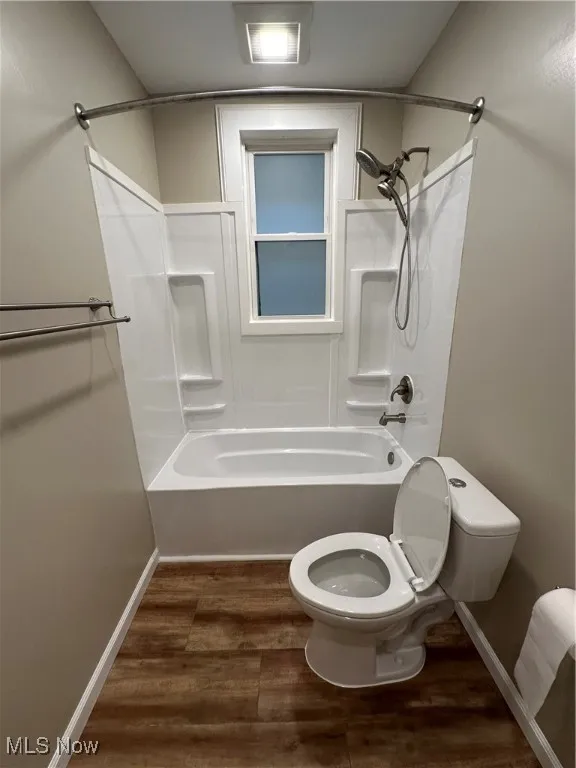Bathroom with hardwood / wood-style floors, tub / shower combination, and toilet