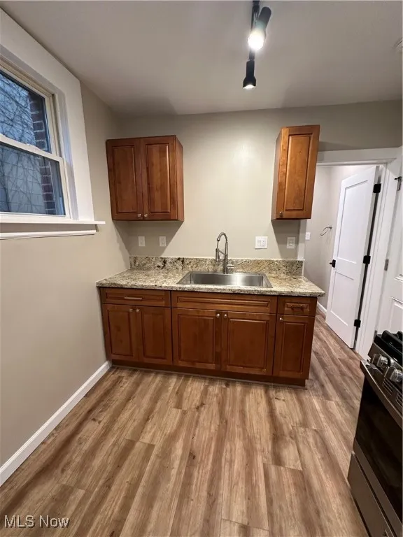 Kitchen featuring sink, light stone countertops, light wood-type flooring, and stove