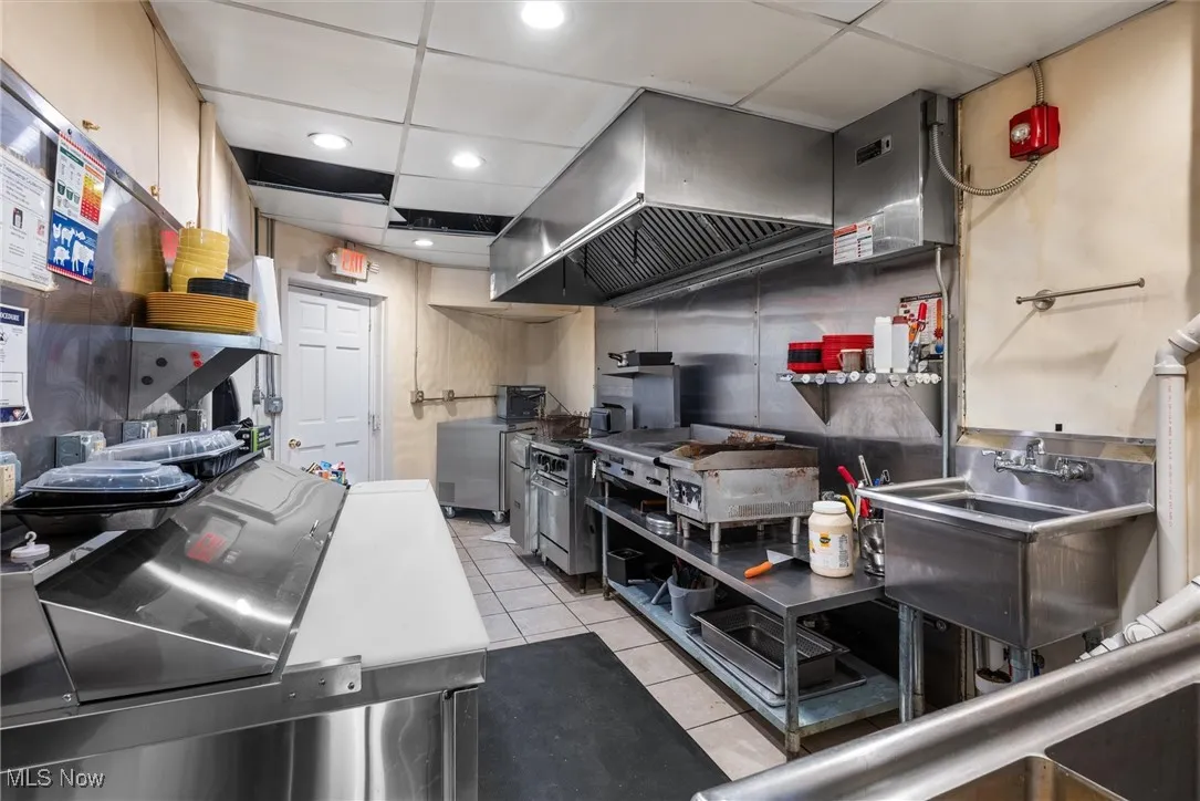 Kitchen featuring light tile patterned flooring, sink, wall chimney exhaust hood, and a paneled ceiling