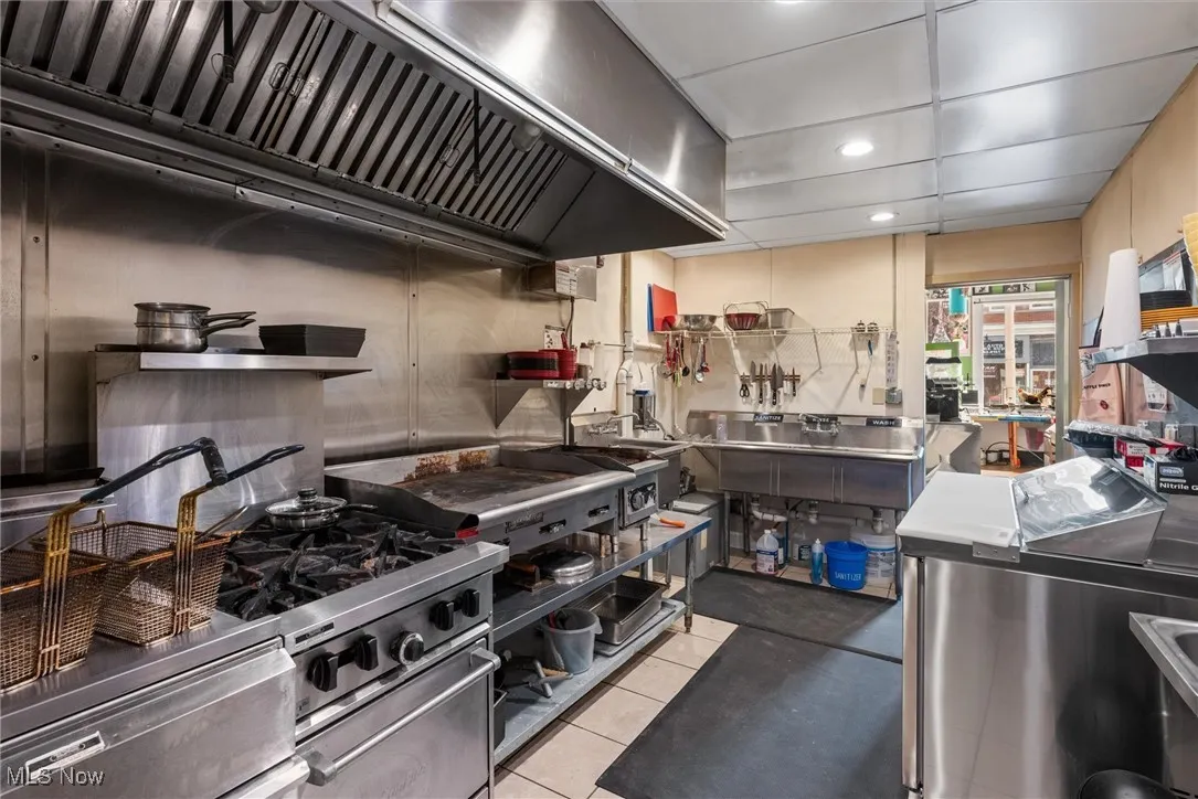 Kitchen with light tile patterned flooring, stainless steel counters, stainless steel stove, and premium range hood