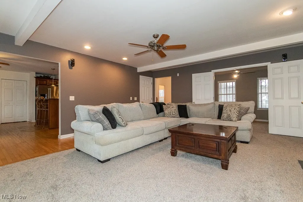 Carpeted living room featuring beam ceiling and ceiling fan