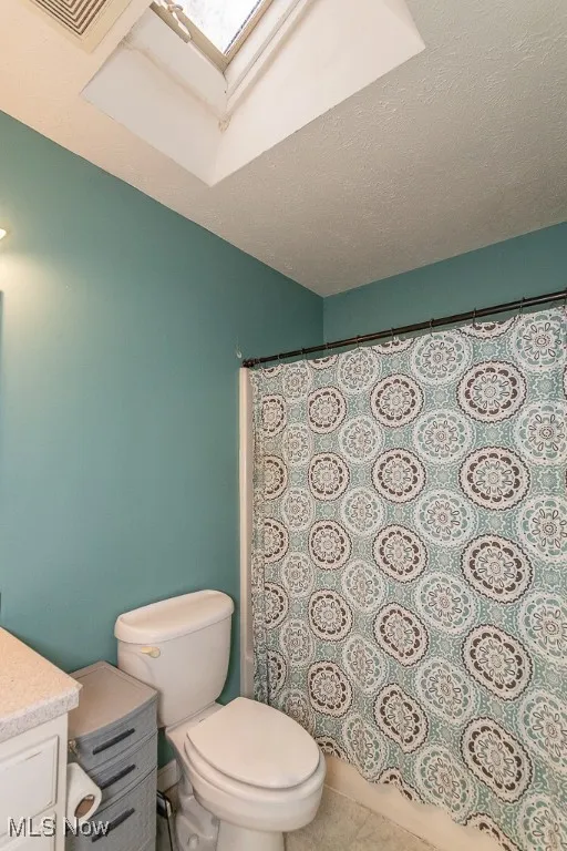 Bathroom featuring tile patterned flooring, vanity, toilet, and a textured ceiling