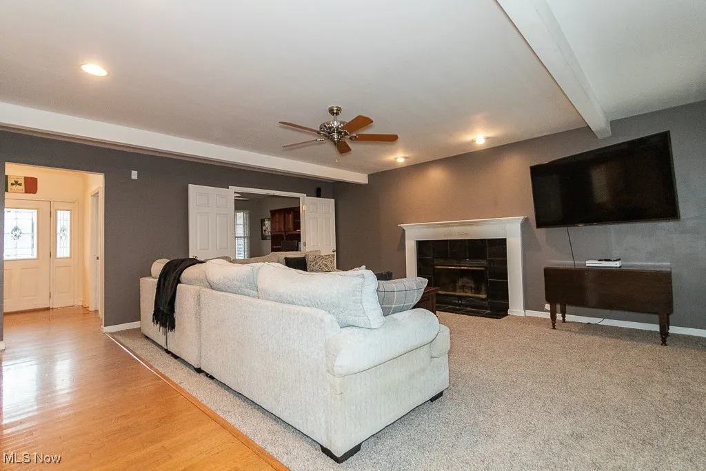 Living room with beam ceiling, a tile fireplace, and ceiling fan