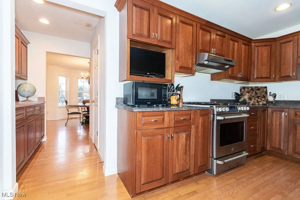 Kitchen with dark stone countertops, stainless steel gas stove, light hardwood / wood-style floors, and an inviting chandelier
