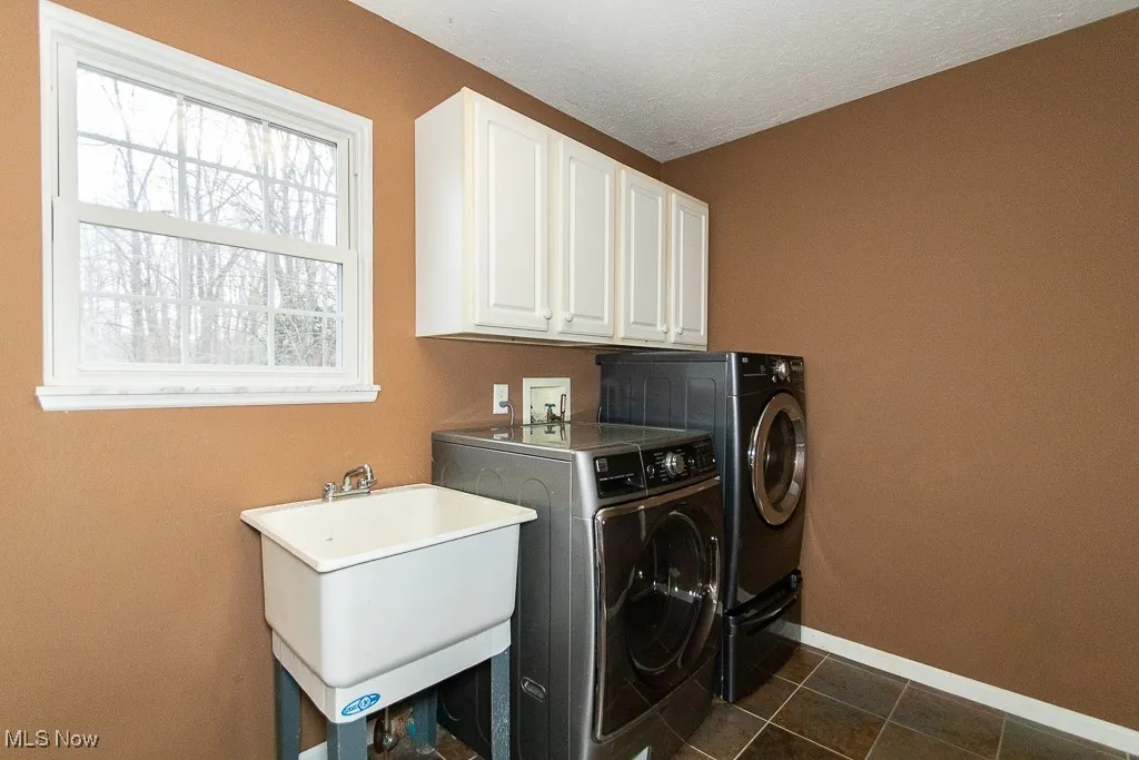 Laundry area featuring cabinets, a textured ceiling, dark tile patterned floors, sink, and washer and dryer